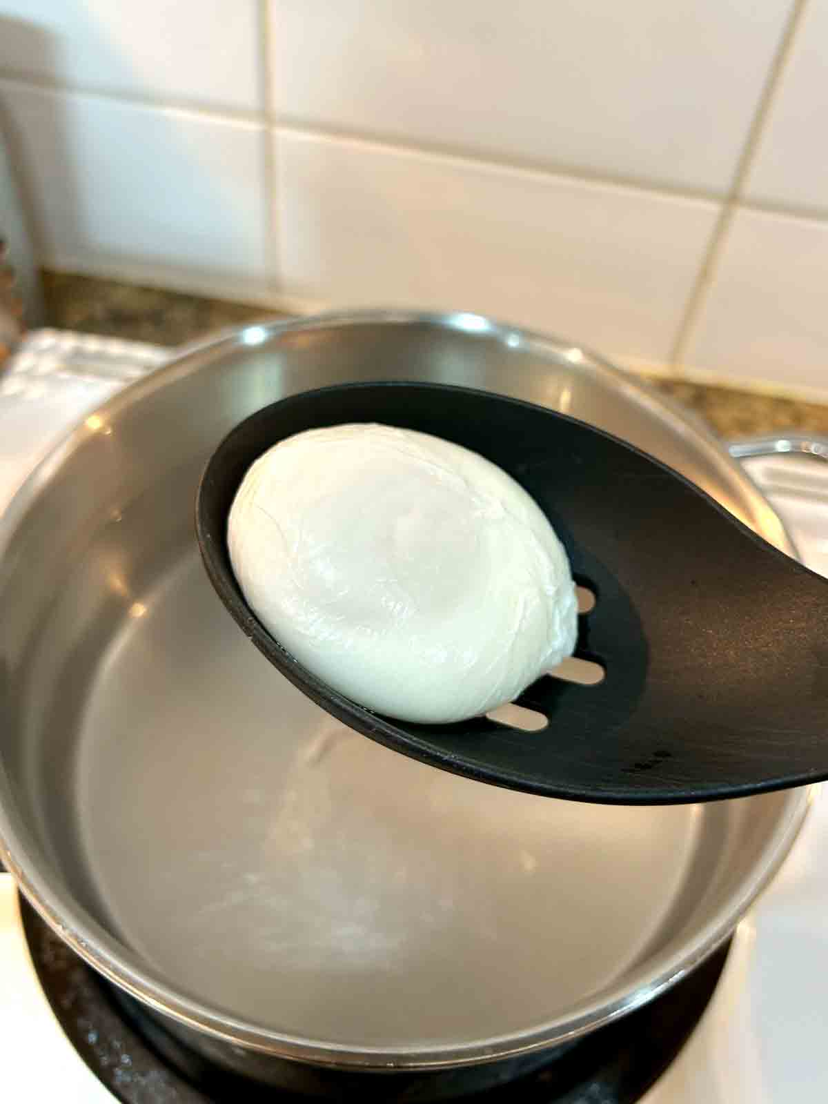 slotted spoon lifting out poached egg from water.