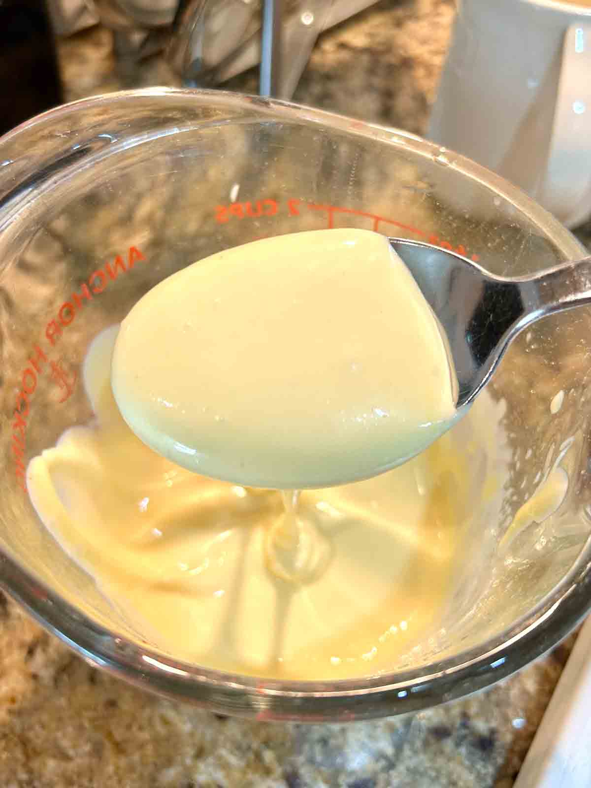 spoon lifting hollandaise sauce from measuring cup.