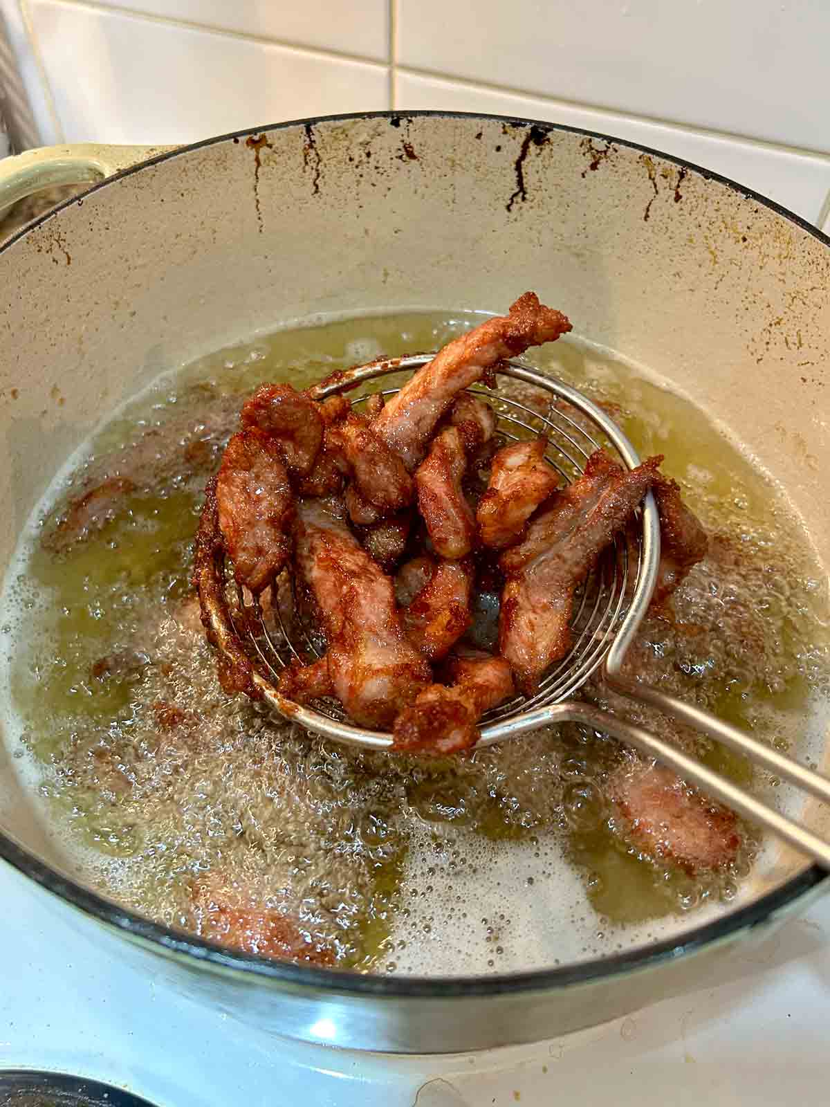 metal spider lifting out deep-fried pork slices from hot oil.