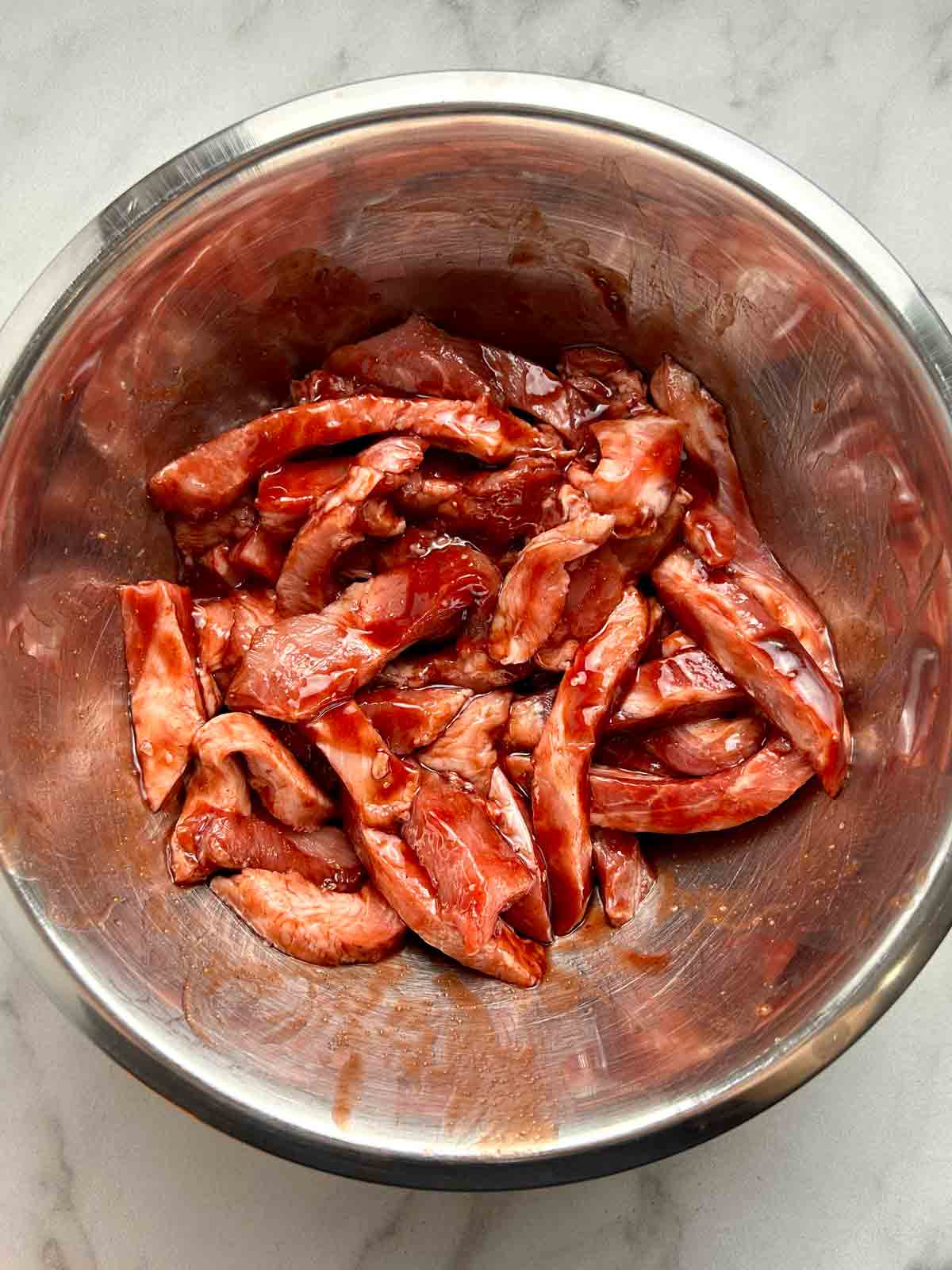 pork shoulder slices being marinated in red sauce in bowl.