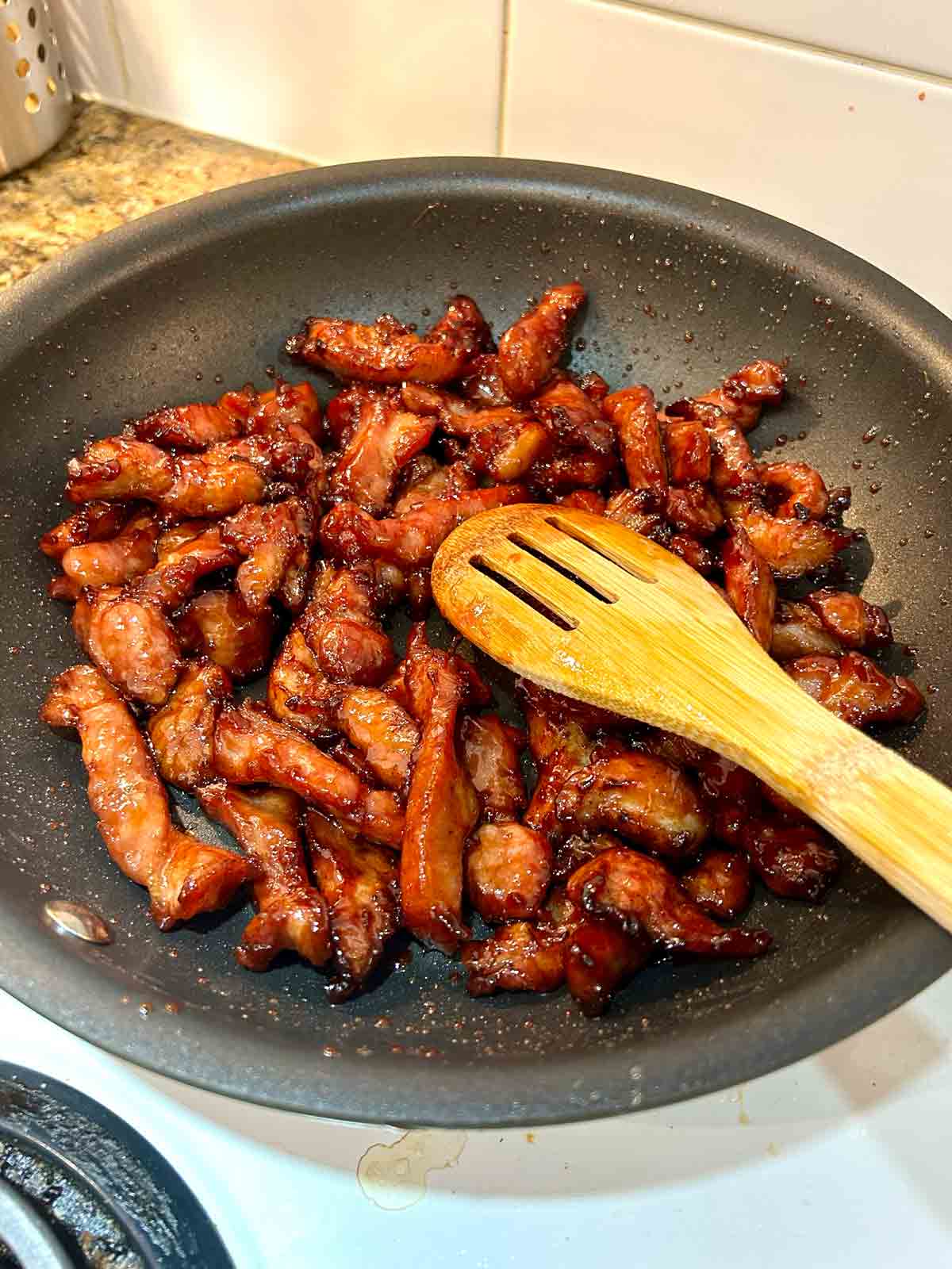 fried pork slices being tossed with glaze in pan.