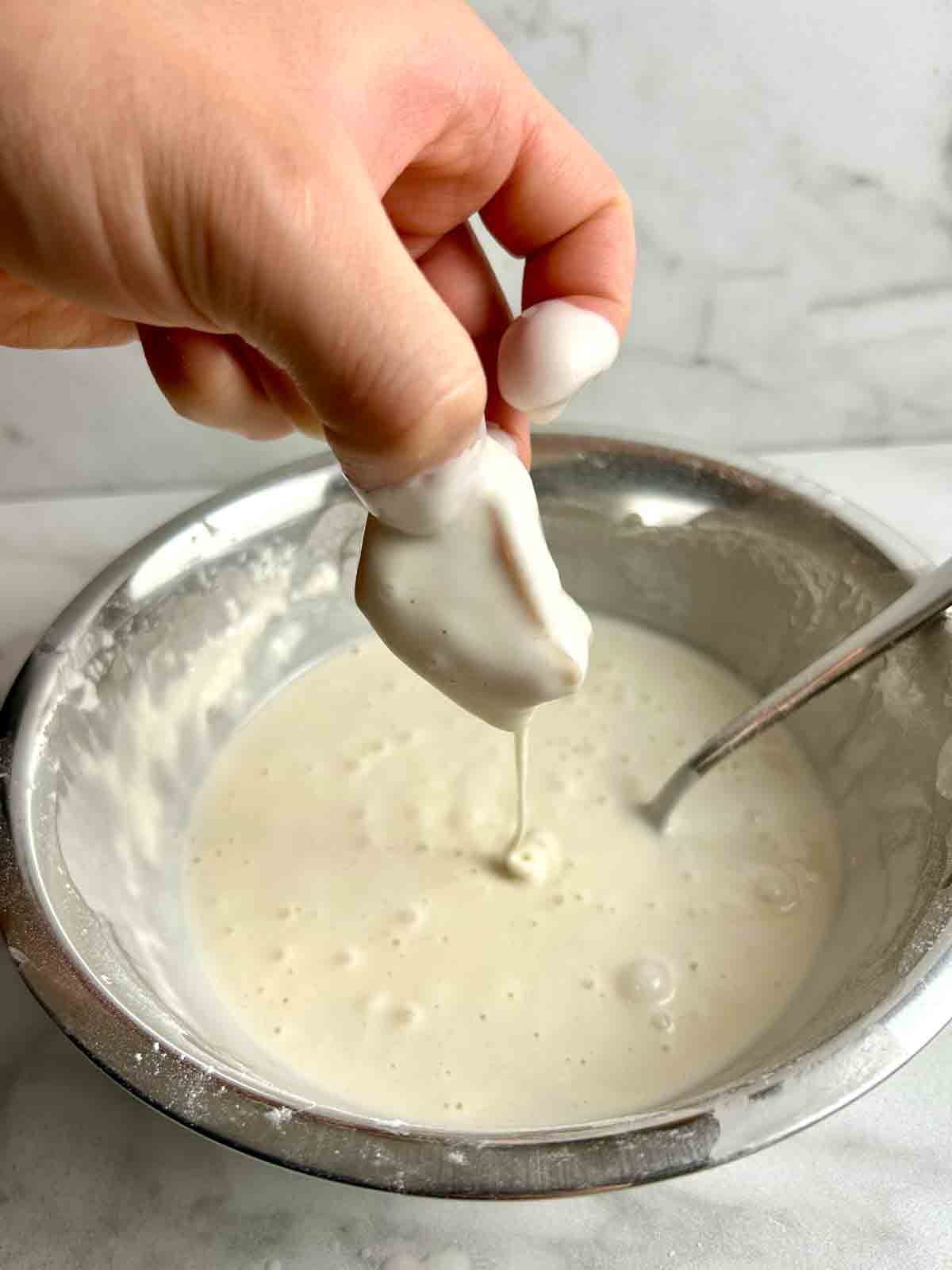 dipping cube of chicken breast into wet batter.