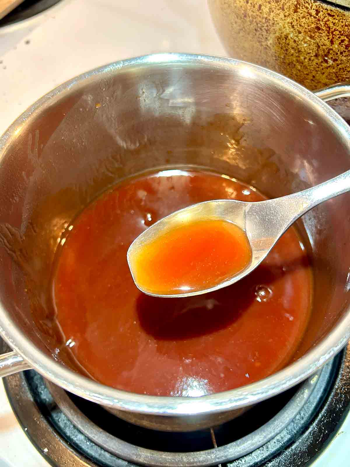 spoon lifting sweet and sour sauce from saucepan.