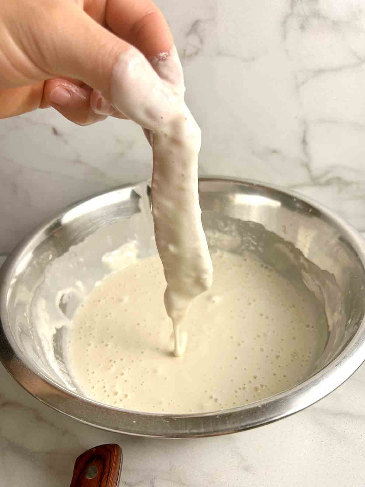 piece of chicken being coated in wet batter.