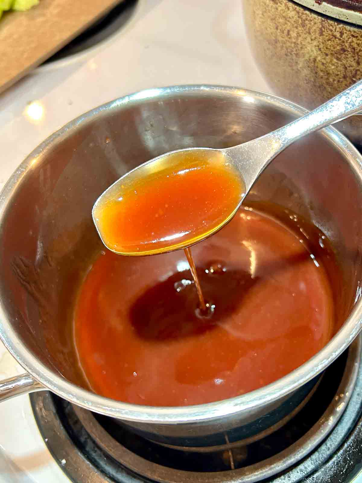 spoon lifting sweet and sour sauce from saucepan.