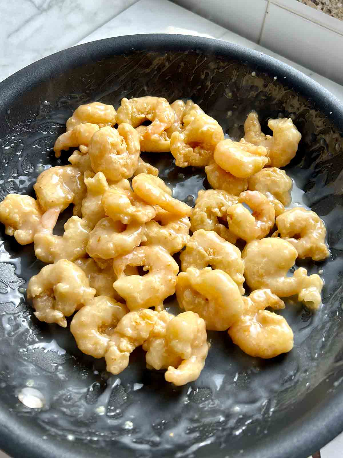 deep fried shrimp tossed with coconut sauce in nonstick pan.