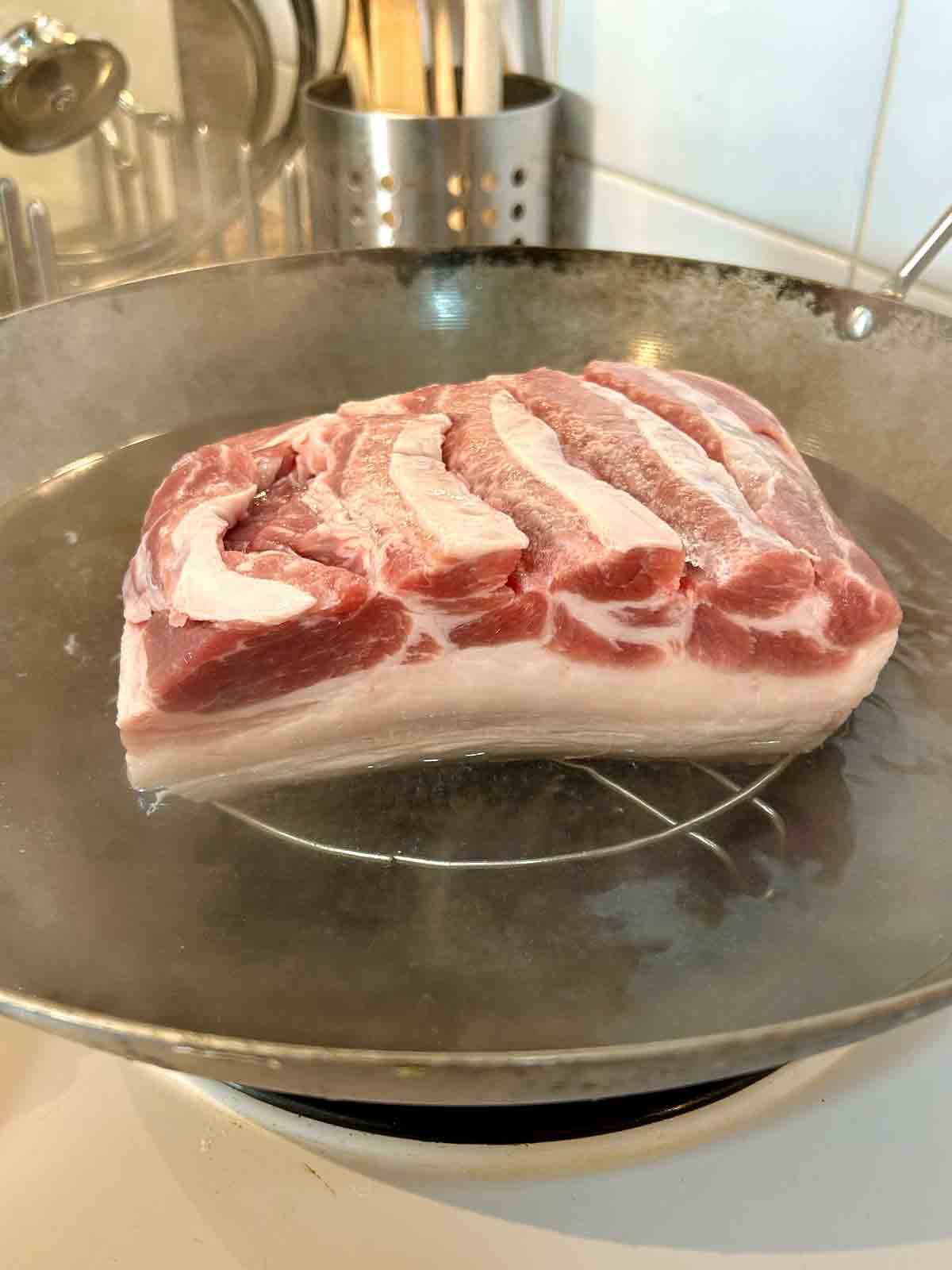 pork belly placed on a rack in boiling water, skin-side down, meat above water.