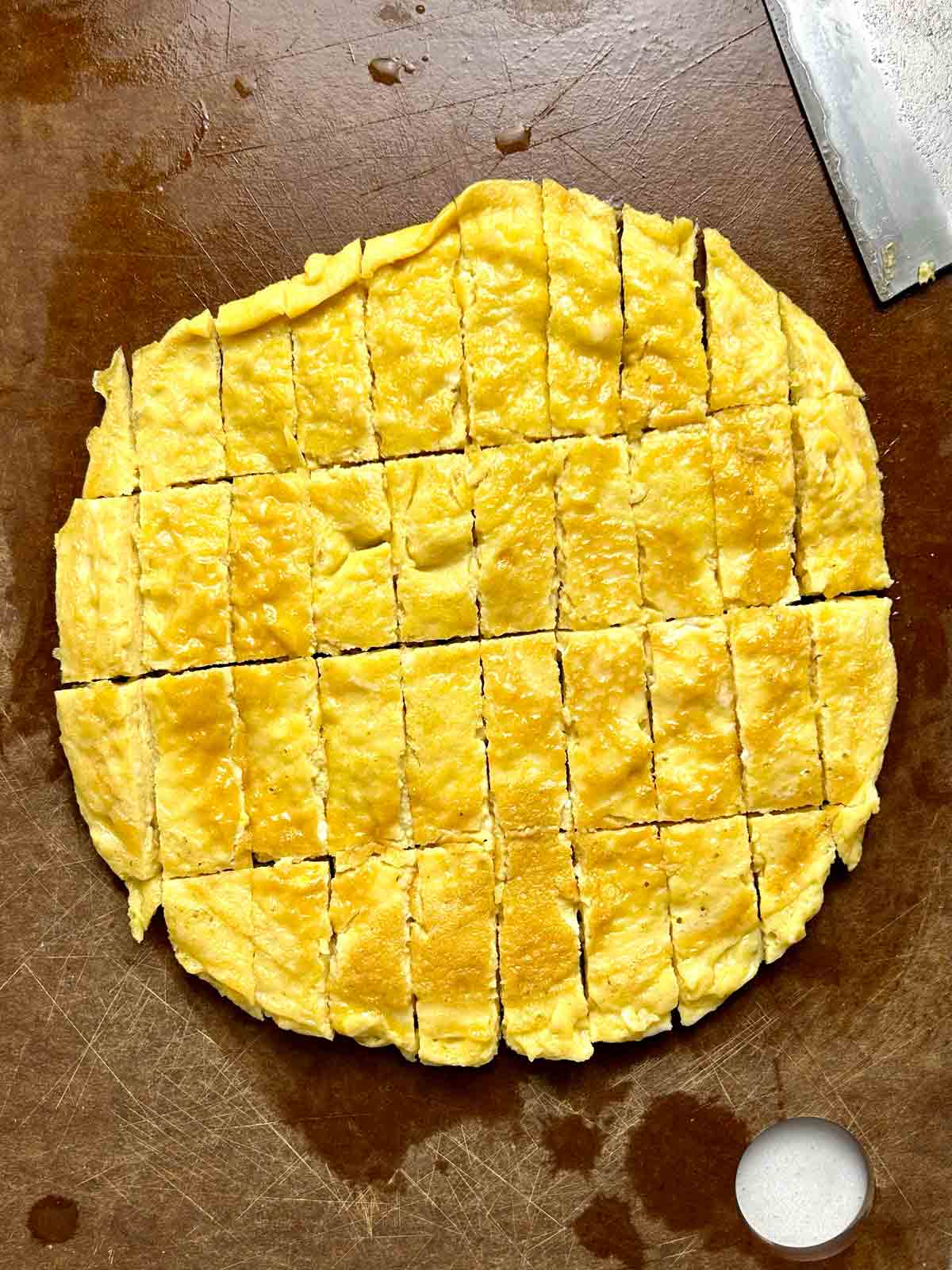 egg omelet being cut into small pieces on cutting board.