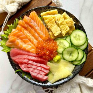 chirashi bowl with salmon, tuna, tamago, ikura, cucumber, pickled ginger, and wasabi.