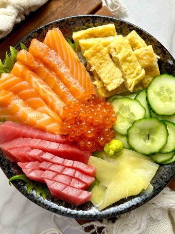 chirashi bowl with salmon, tuna, tamago, ikura, cucumber, pickled ginger, and wasabi.