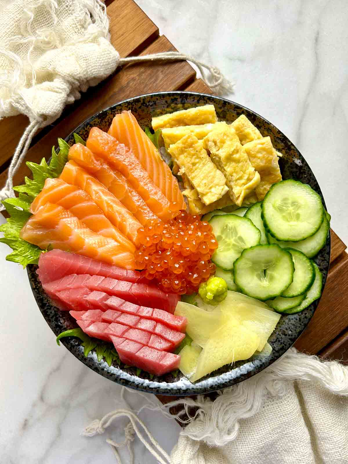 chirashi bowl with salmon, tuna, tamago, ikura, cucumber, pickled ginger, and wasabi.