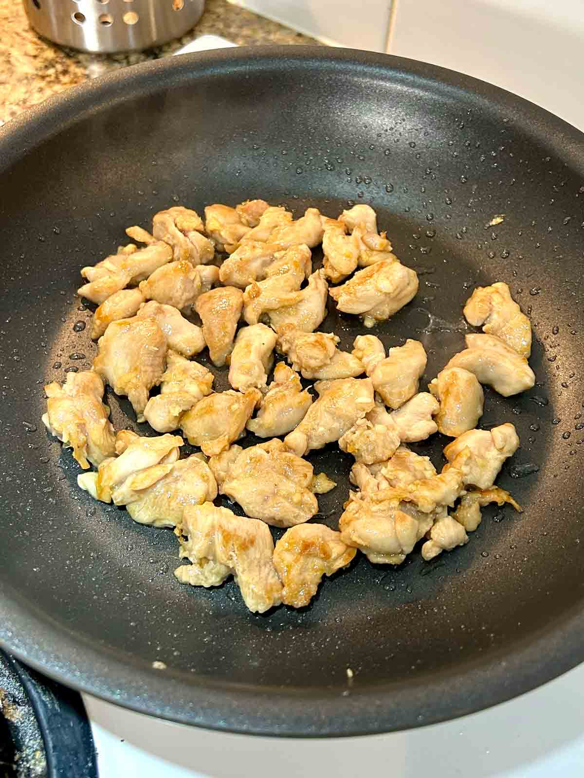 pieces of chicken being stir-fried in nonstick pan.