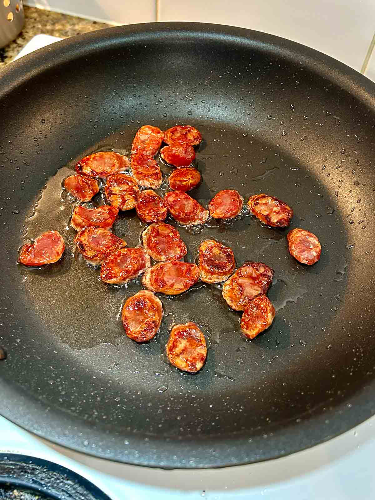 slices of Chinese sausage being stir fried in pan.