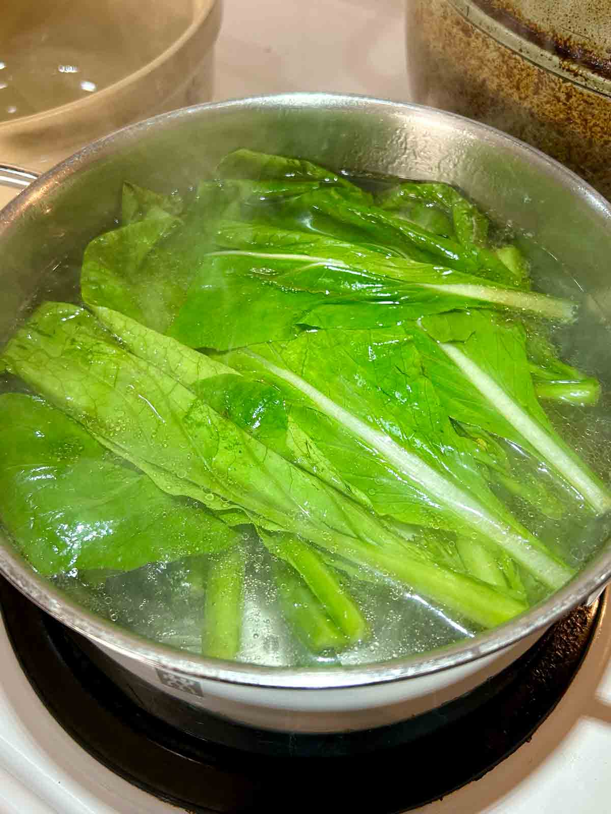 yu choy being boiled in pot of water.