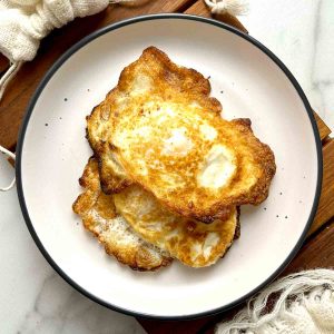 two fried eggs with crispy brown bottoms on a plate.