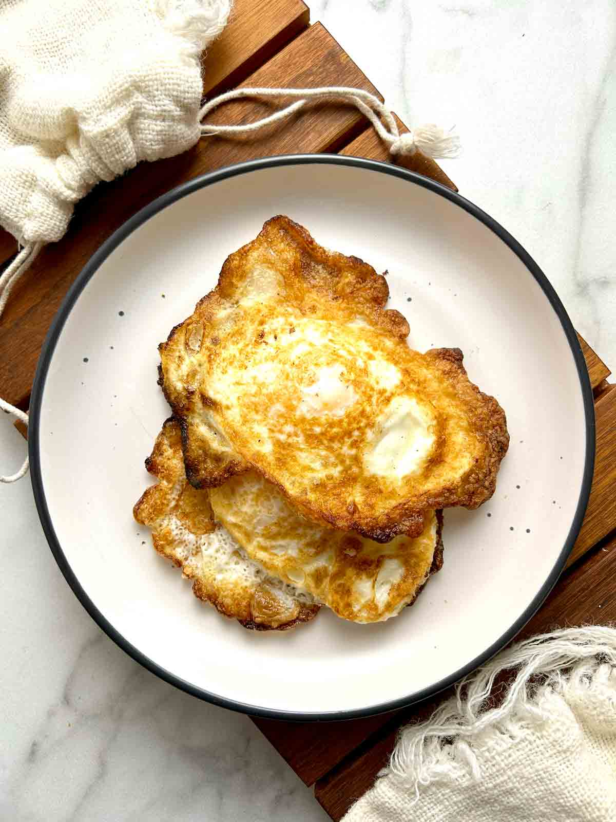 two fried eggs with crispy brown bottoms on a plate.