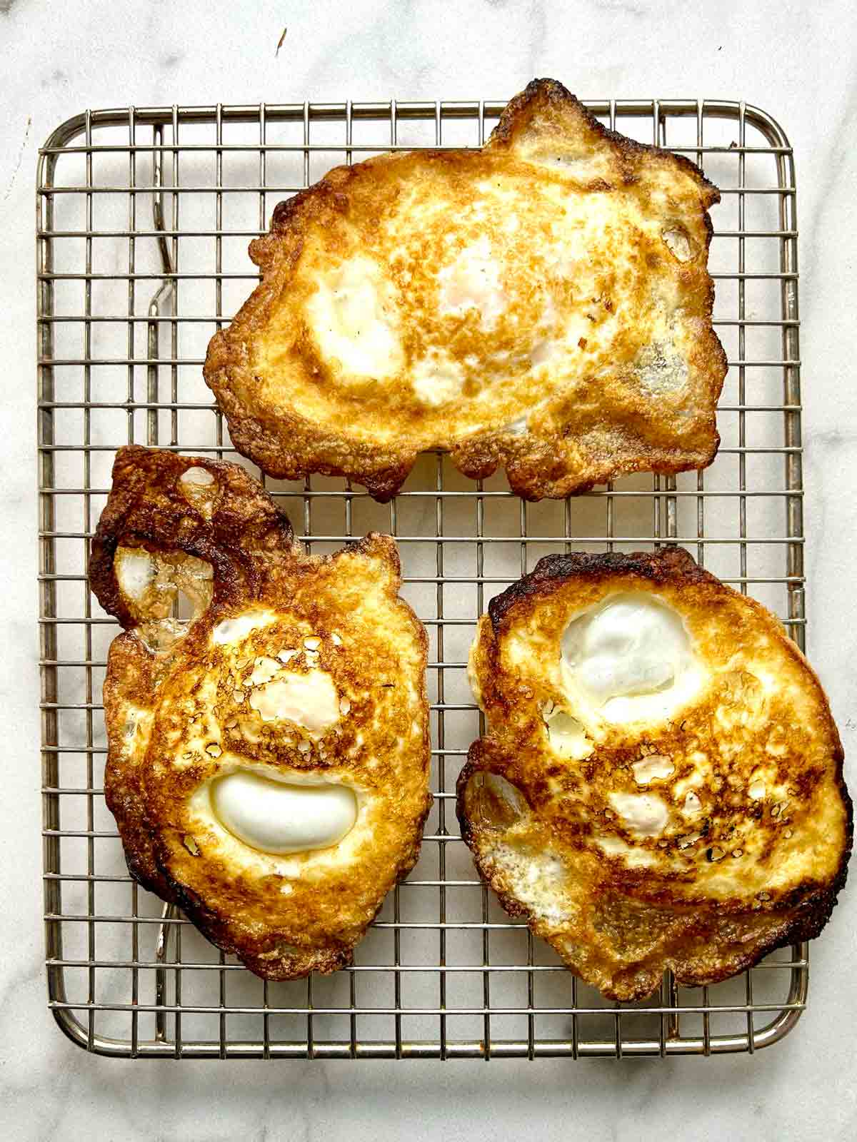 three pan-fried eggs resting on wire rack.