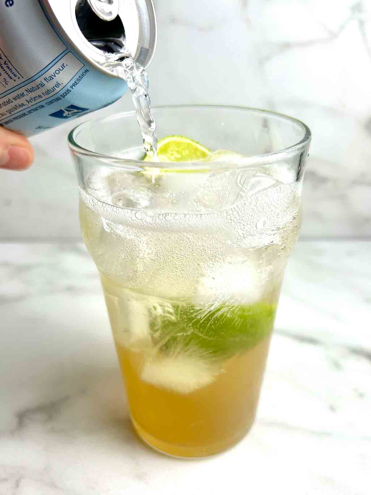 canned sparkling water being poured into cup of ginger ale.