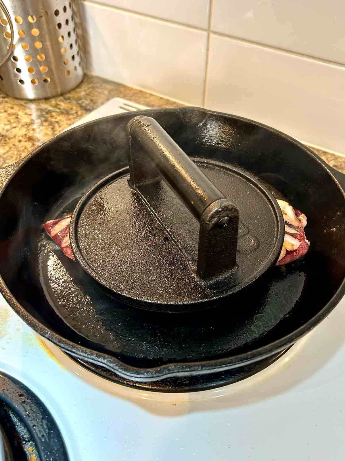 smash burger press placed on top of squid head to keep it in contact with pan.