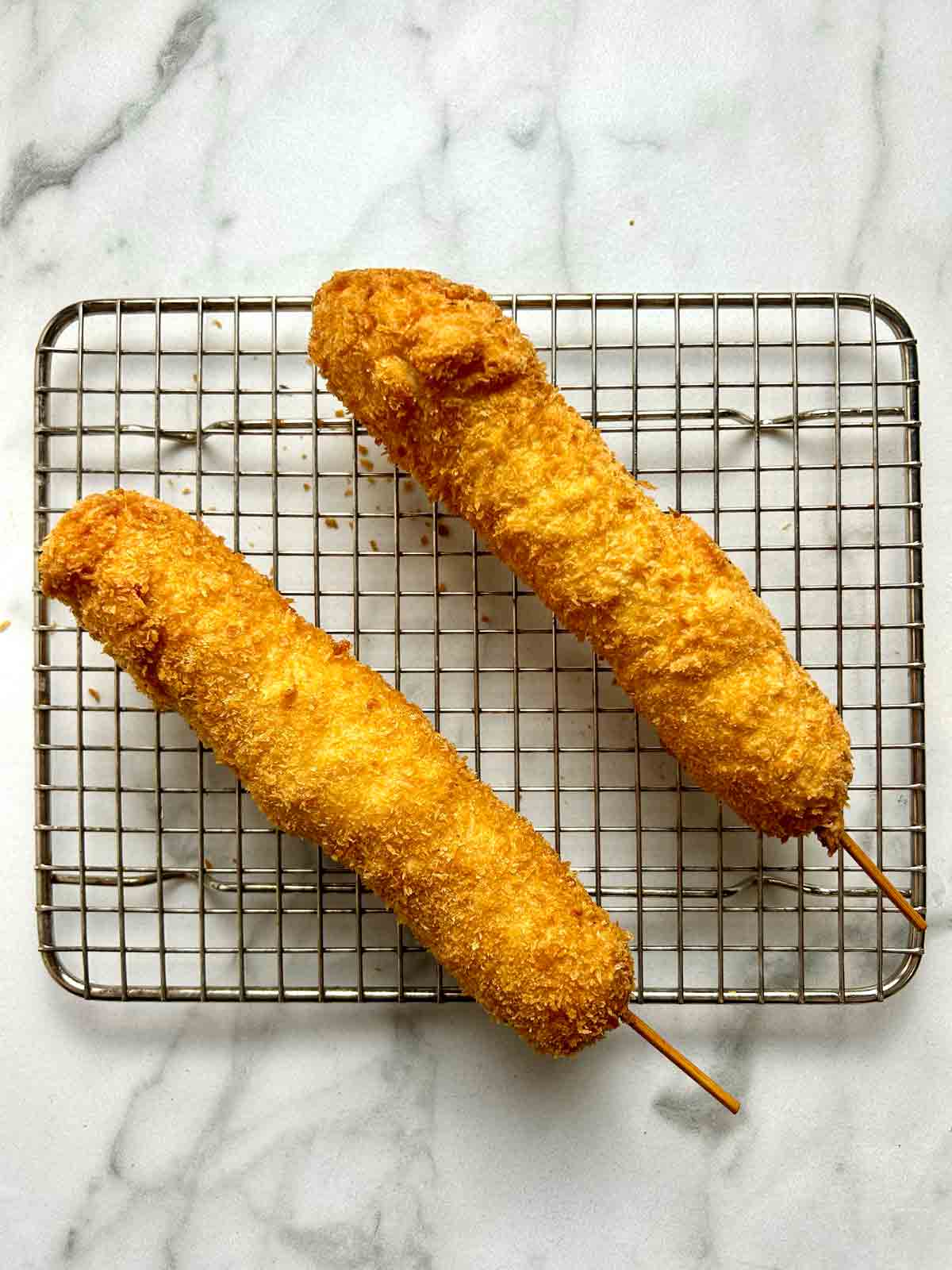 two Korean corn dogs drying on wire rack.