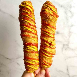 hand holding two Korean corn dogs covered with ketchup and mustard.