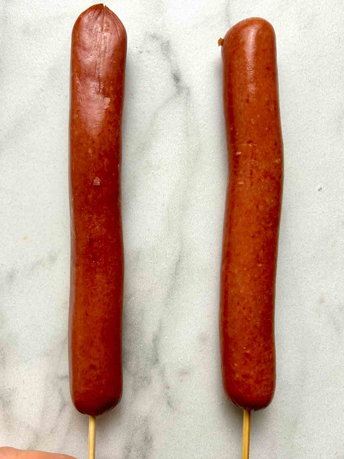 two hot dogs skewered onto bamboo sticks.