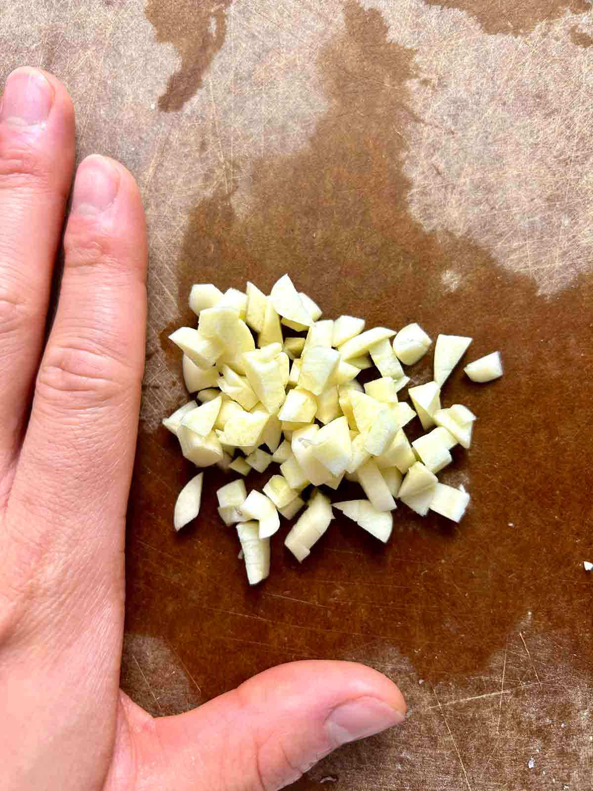 chopped garlic on cutting board with hand as reference.