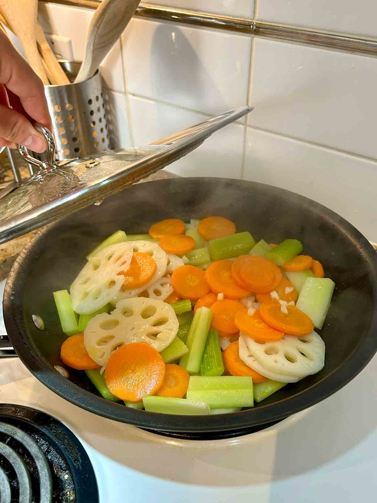 lid being lifted off pan with vegetables cooking inside it.