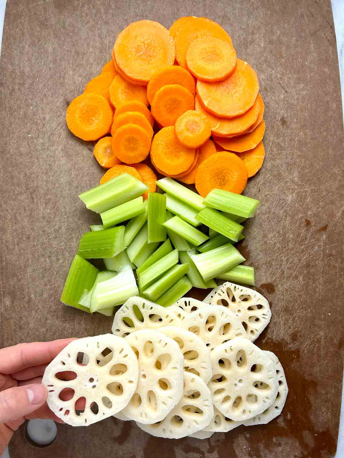 slices of carrots, celery, and lotus root in separate piles on a cutting board.