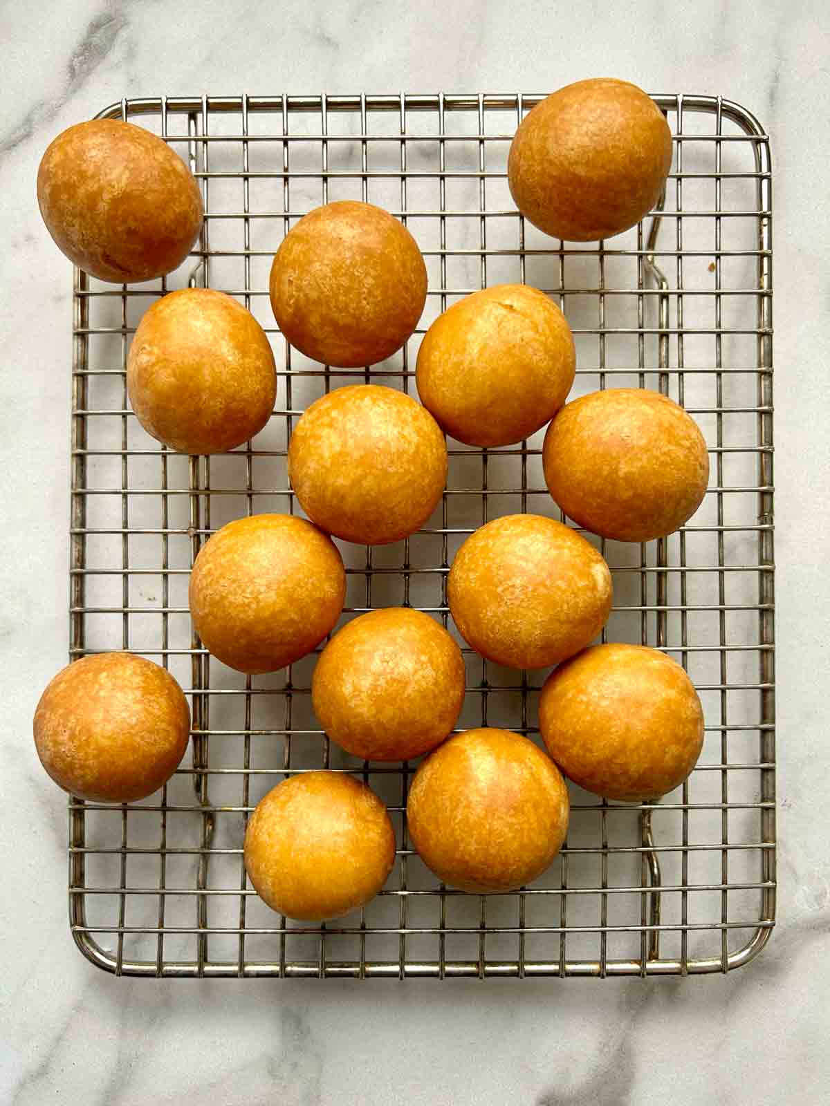 fried mochi donut holes drying on wire rack.