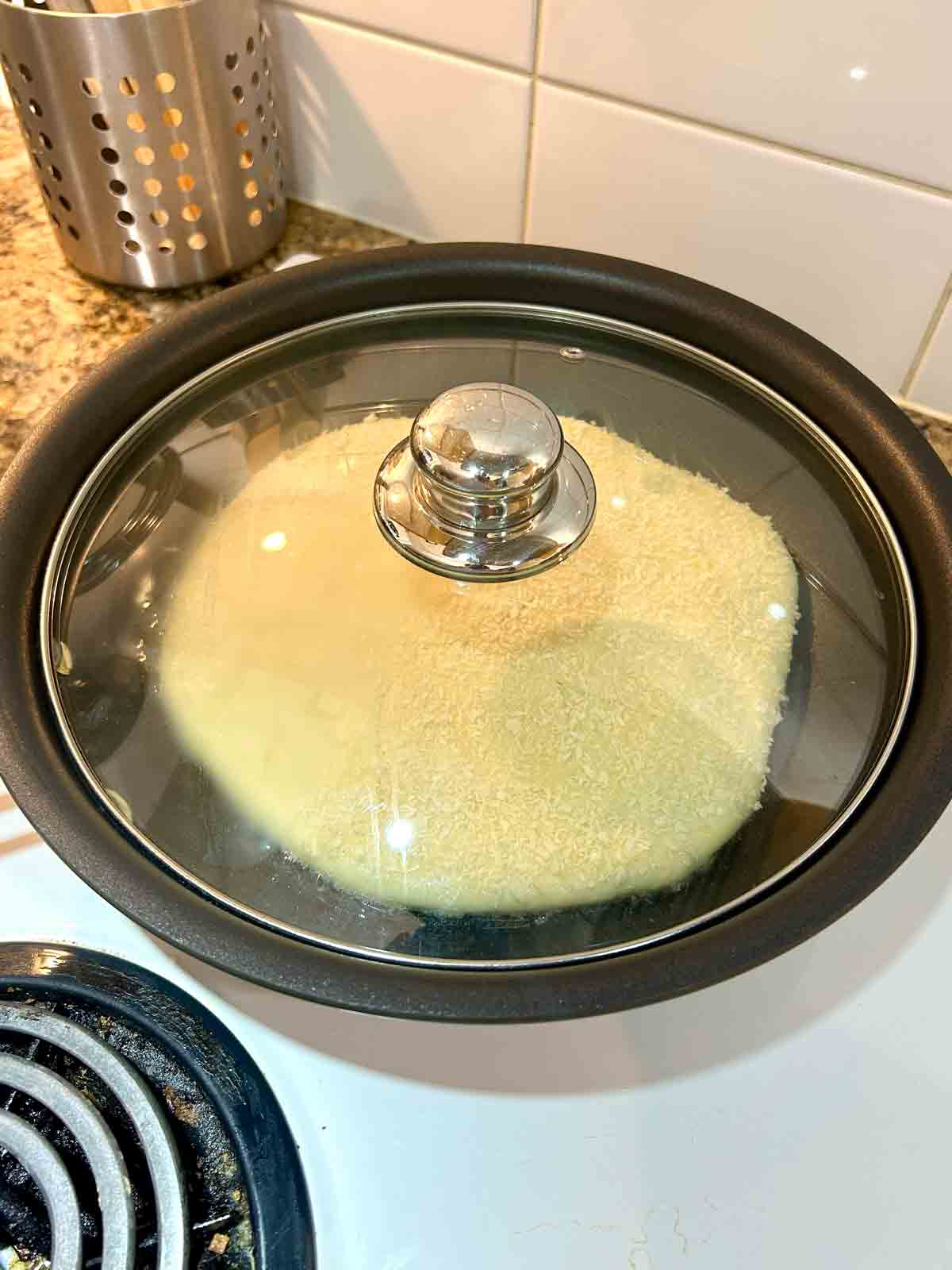 dough being pan-fried with lid on top.