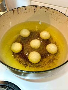 sesame balls sitting at bottom of oil in pot.