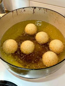 golden brown sesame balls floating in oil.