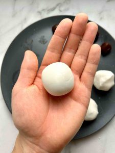 hand holding rolled ball of dough with filling inside.