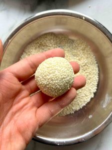 dough being rolled in sesame seeds.