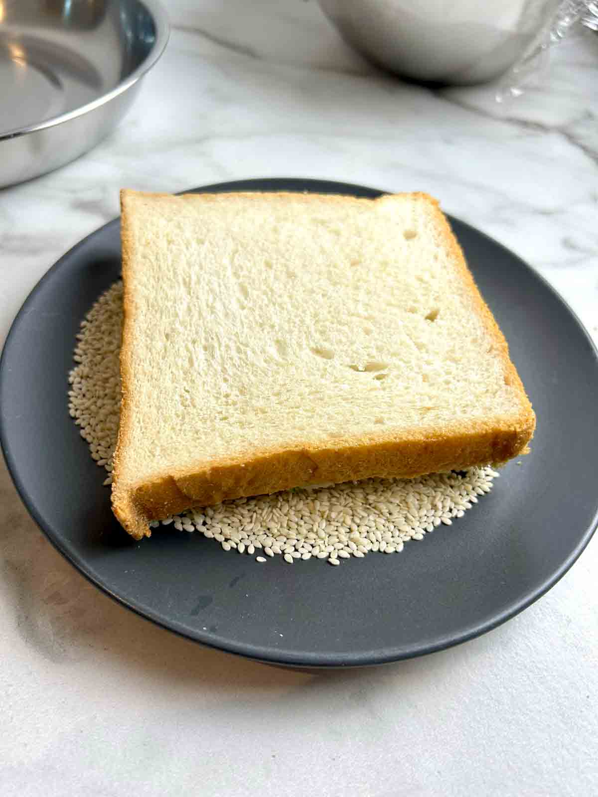 bread being pressed into plate of sesame seeds.