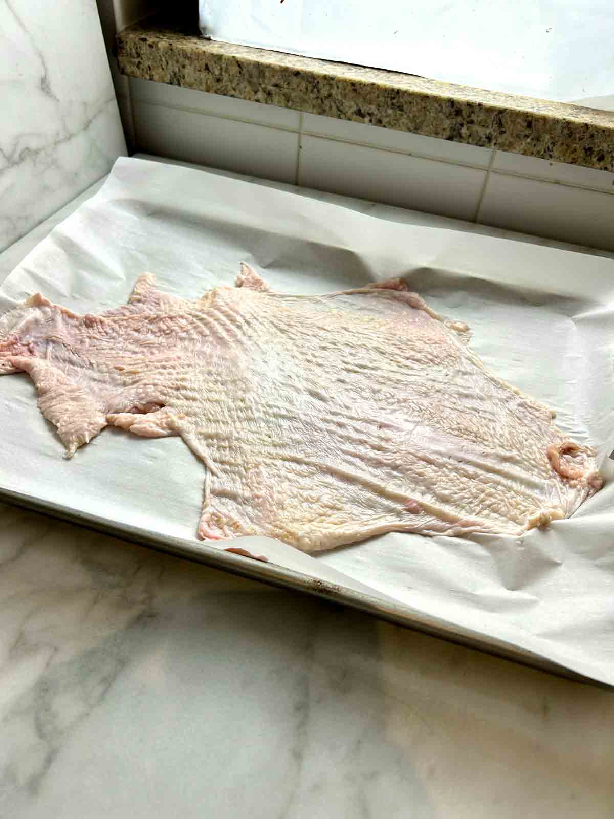 turkey skin placed on top of parchment lined baking sheet.