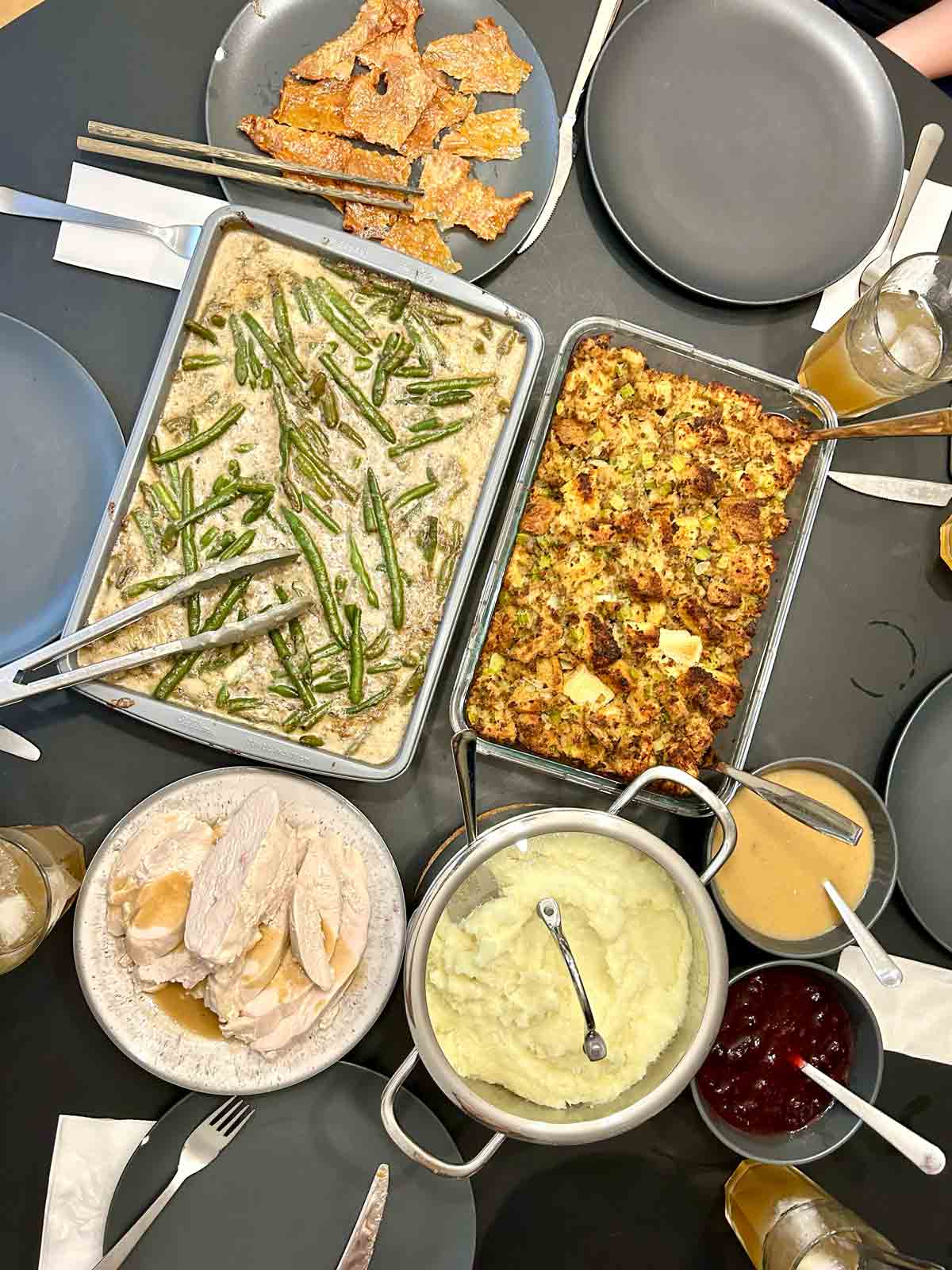 overhead shot of Thanksgiving spread containing crispy turkey skin, sous vide turkey breast, green bean casserole, stuffing, mashed potatoes, gravy, and cranberry sauce.