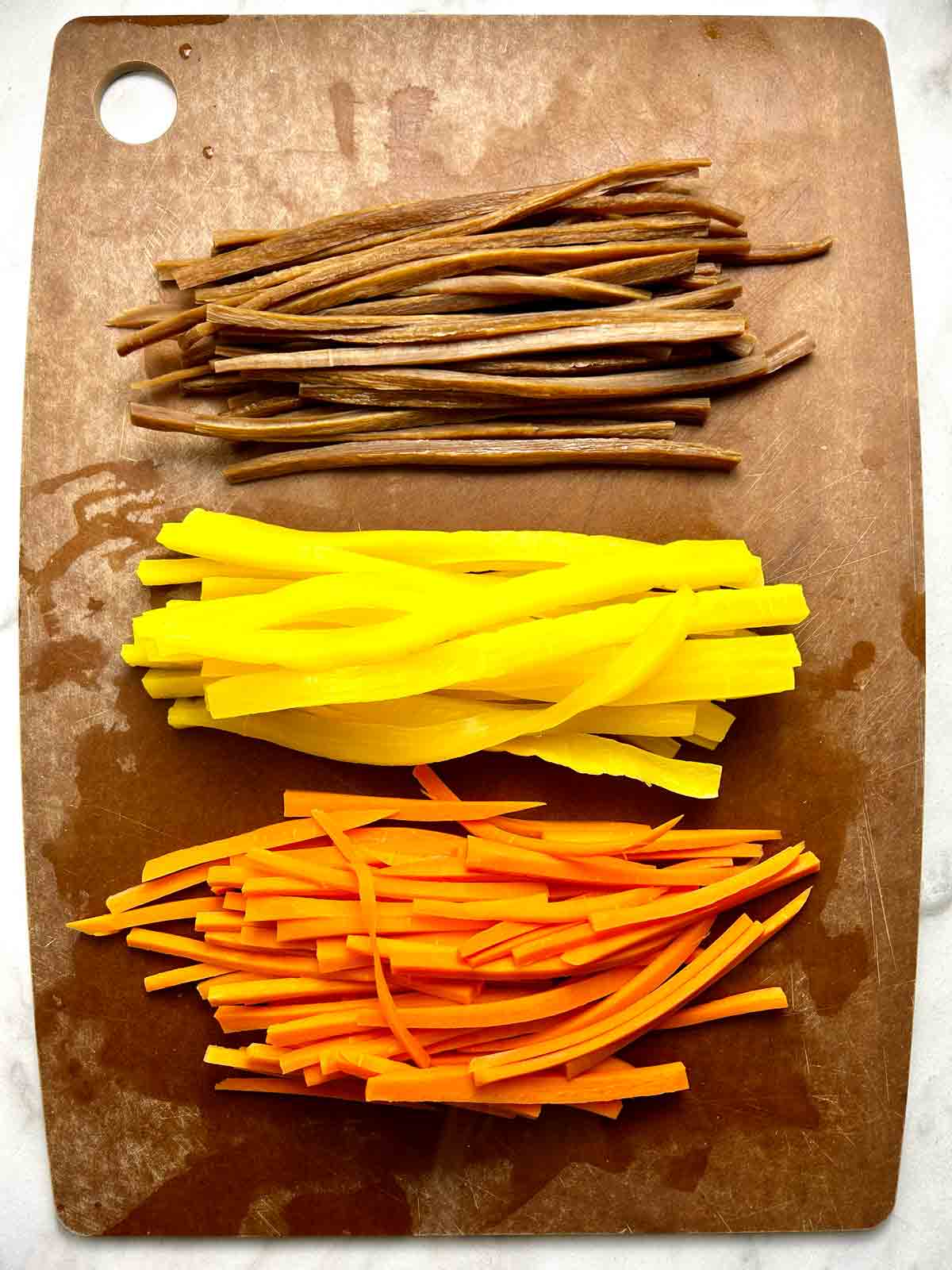 sliced burdock root, yellow pickled radish, and boiled carrots on cutting board.