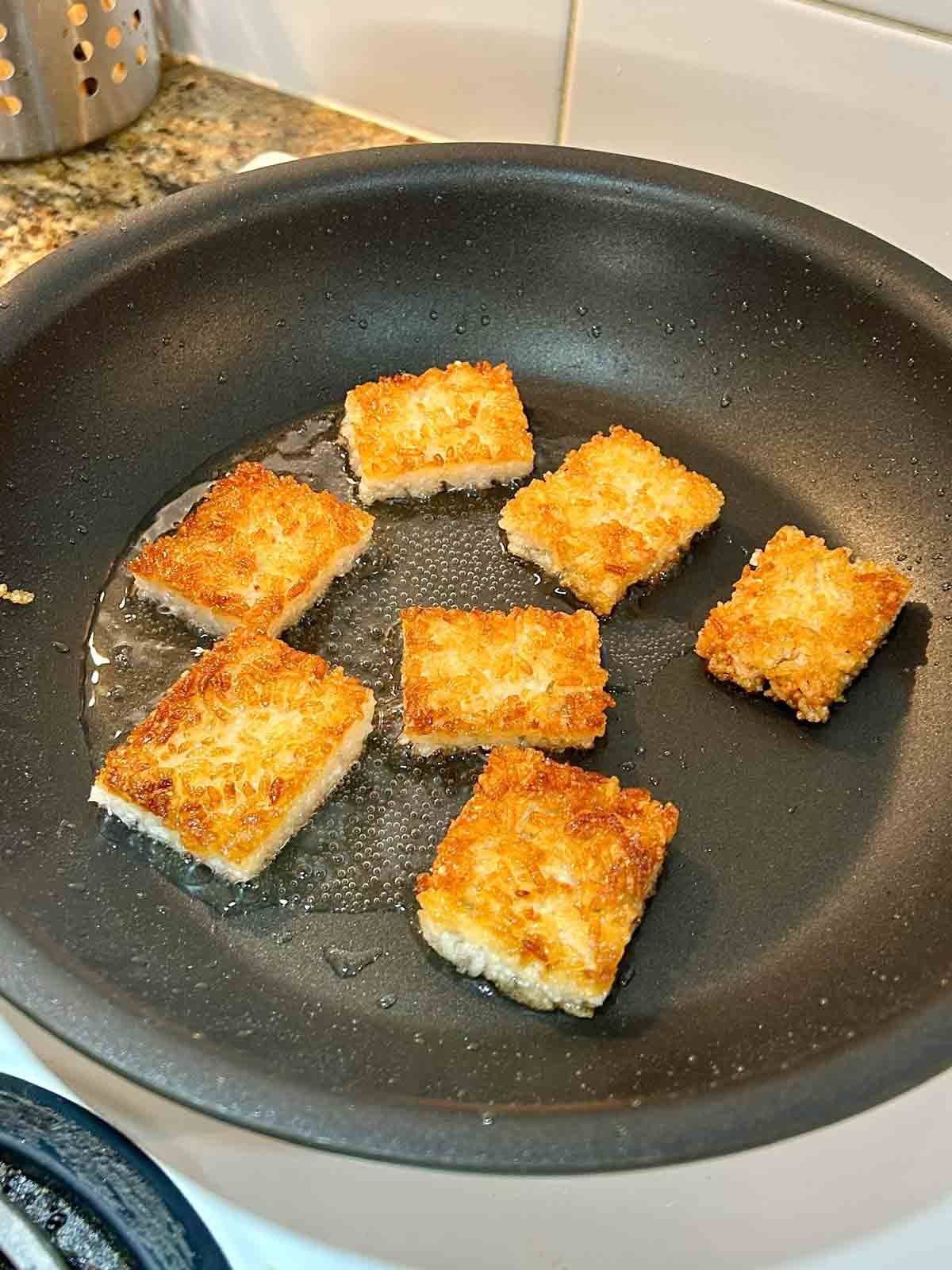 second side of rice rectangles being pan-fried; first side is golden brown.