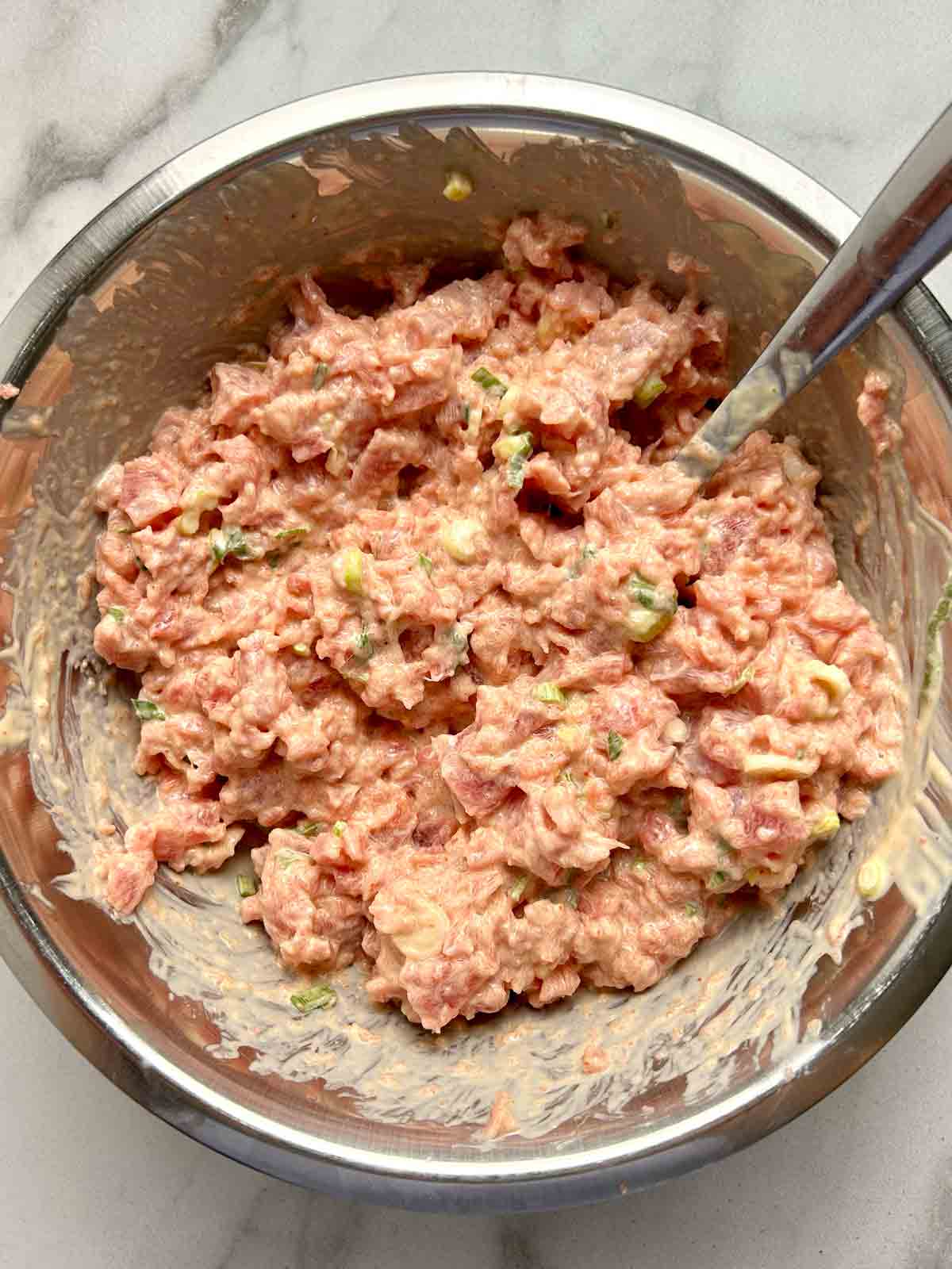 minced raw tuna mixed with sauce ingredients in bowl.