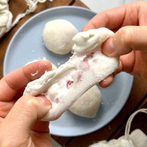 strawberry mochi being torn apart to show filling on the inside.