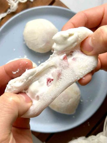 strawberry mochi being torn apart to show filling on the inside.