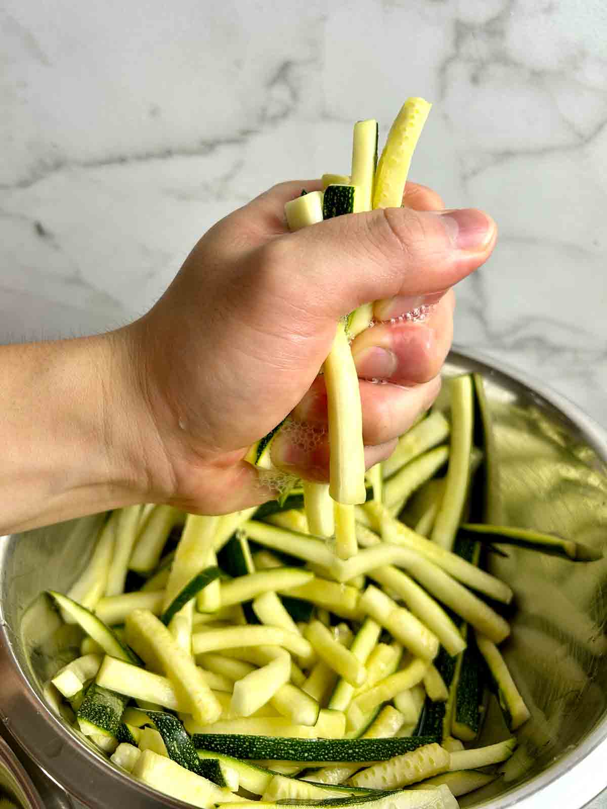 handful of zucchini matchsticks being squeezed dry with hands.