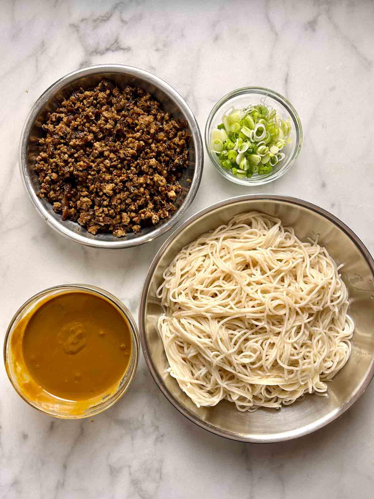 all noodle components in separate bowls; pork topping, slices scallions, sauce, and cooked noodles.