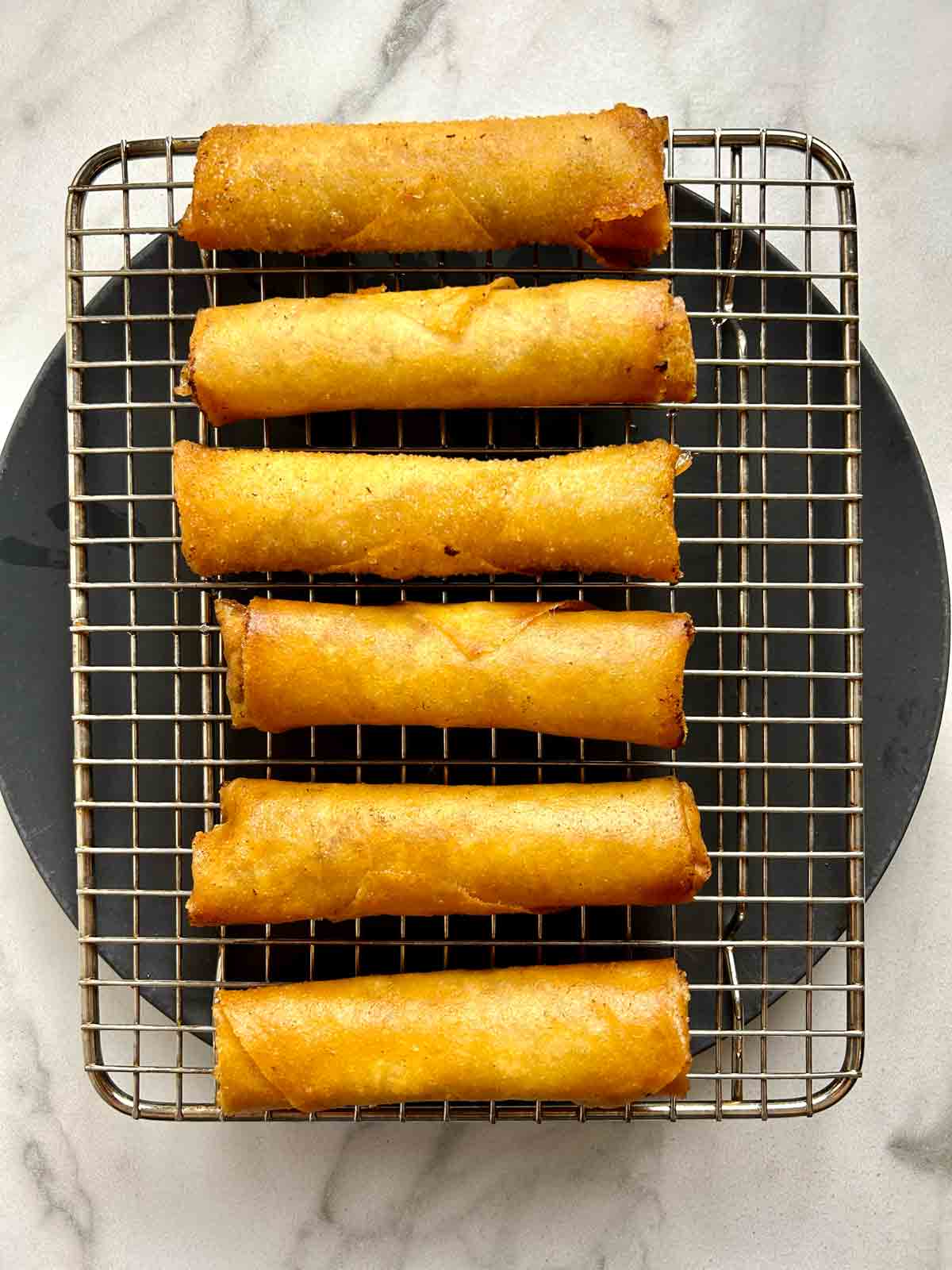 fried spring rolls drying on wire rack.