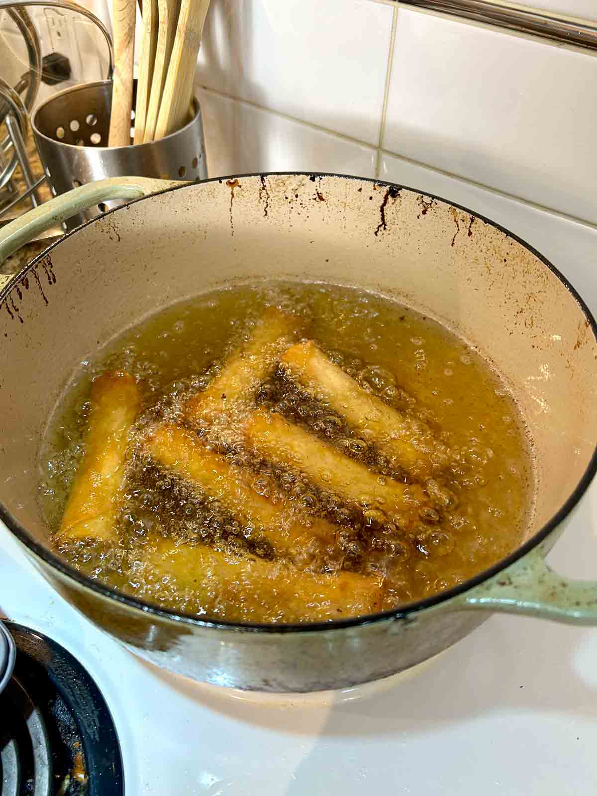 spring rolls being fried in hot oil in Dutch oven.