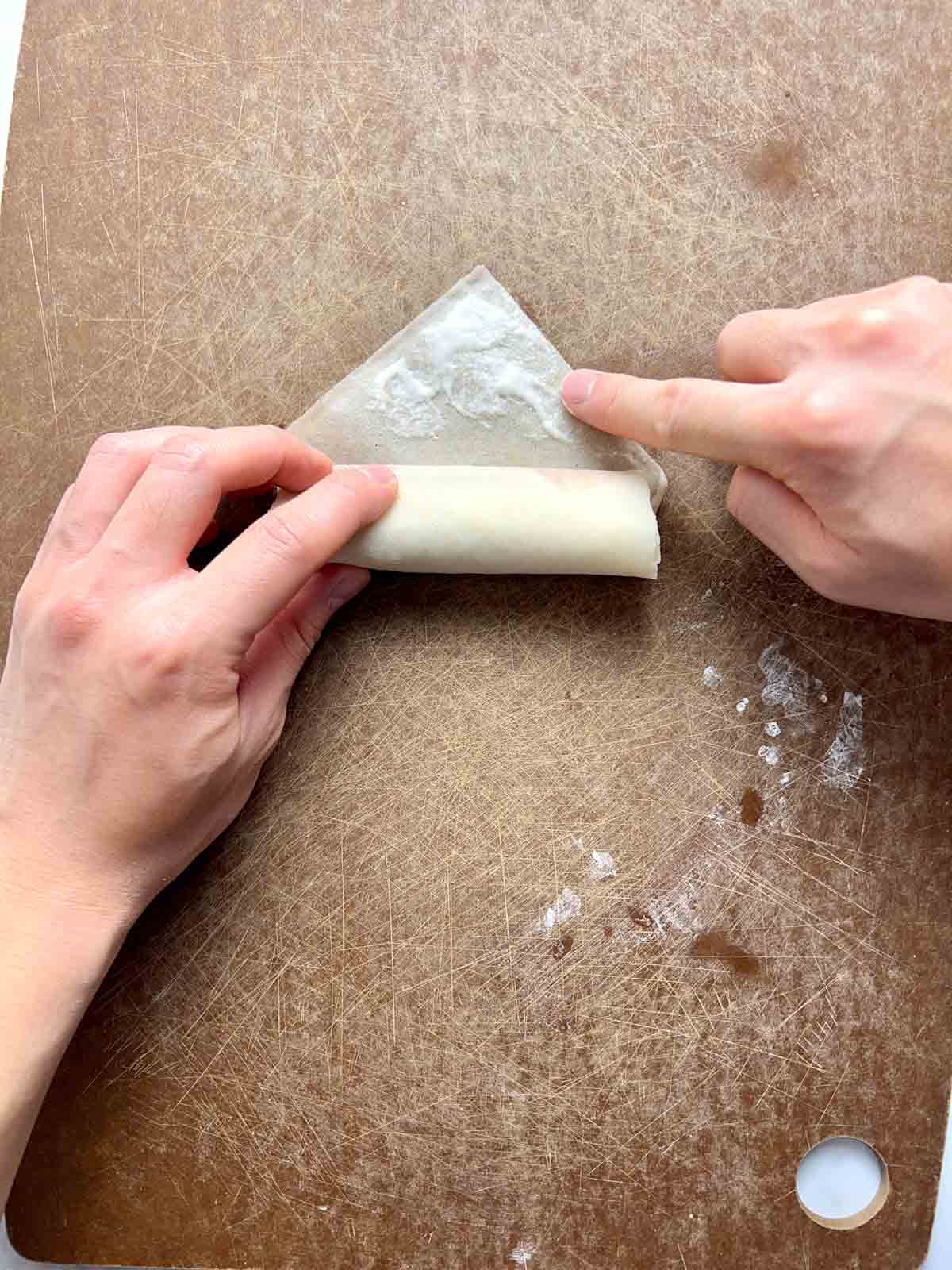 flour paste being applied to top edge of spring roll wrapper.