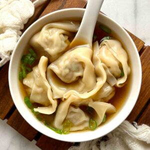 bowl of wonton soup garnished with scallions.