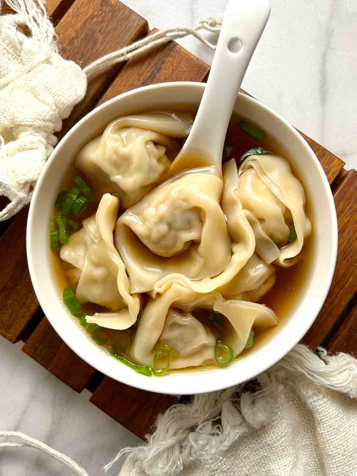 bowl of wonton soup garnished with scallions.